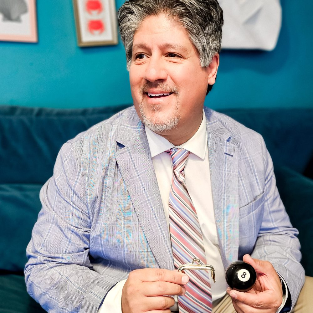 Frank Greer a professional magician, doing hand trick performing for weddings, corporate and special events, blending mind-reading and illusion, dressed in a light blue blazer and striped tie.