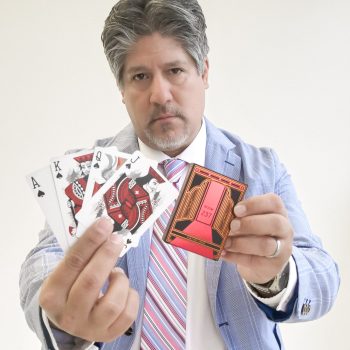 Frank Greer a professional magician, holding a magic card performing for weddings, corporate and special events, blending mind-reading and illusion, dressed in a light blue blazer and striped tie.