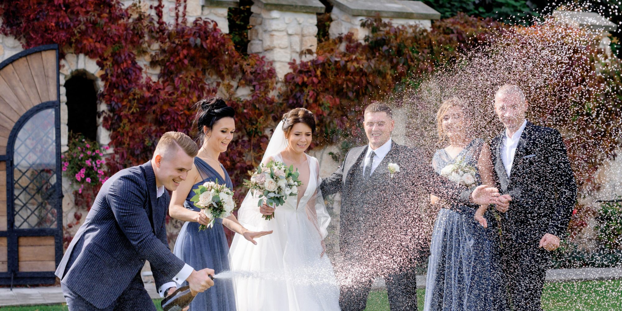Happy bridesmaids, best men and wedding couple is celebrating wedding day outdoors with pouring out champagne