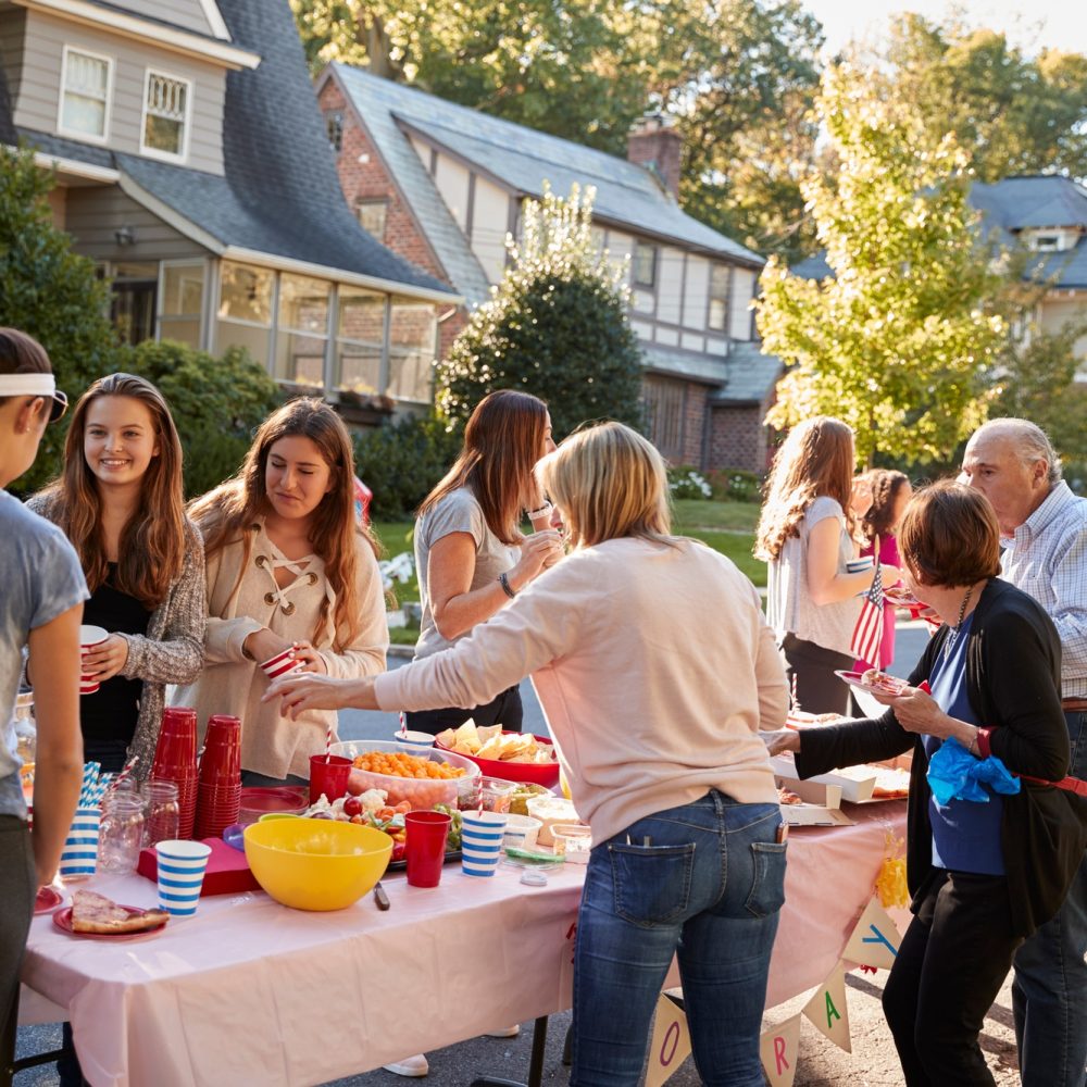 Neighbours talk standing around a table at a block party