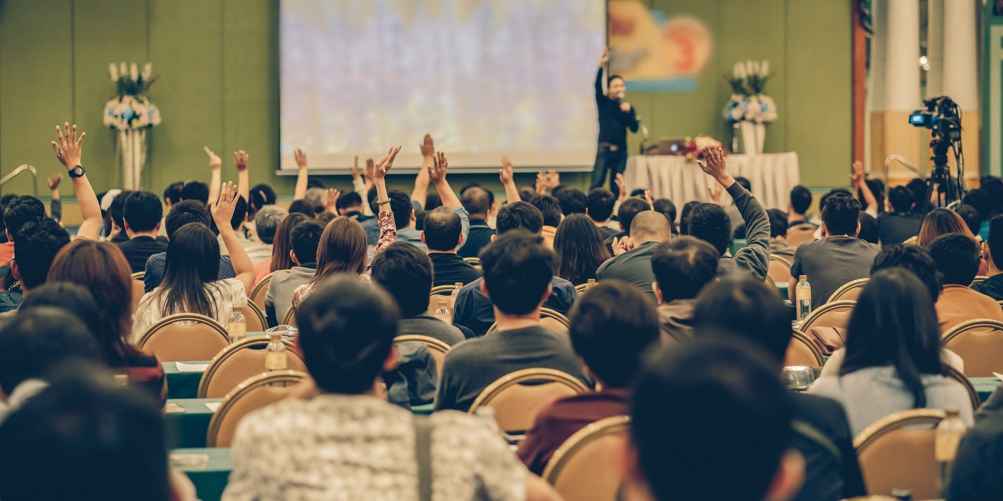 Rear view of Audience showing hand to answer the question from Speaker on the stage